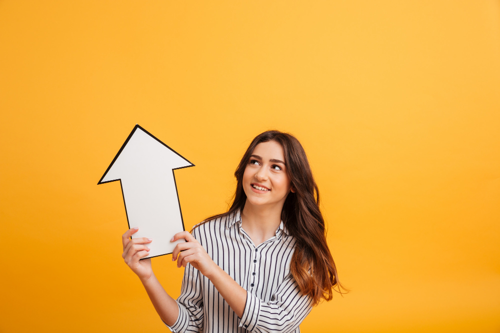 Smiling woman holding an upward arrow sign against a yellow background.
