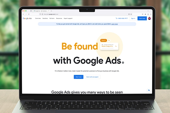 Laptop screen displaying Google Ads homepage with "Be found with Google Ads" text.
